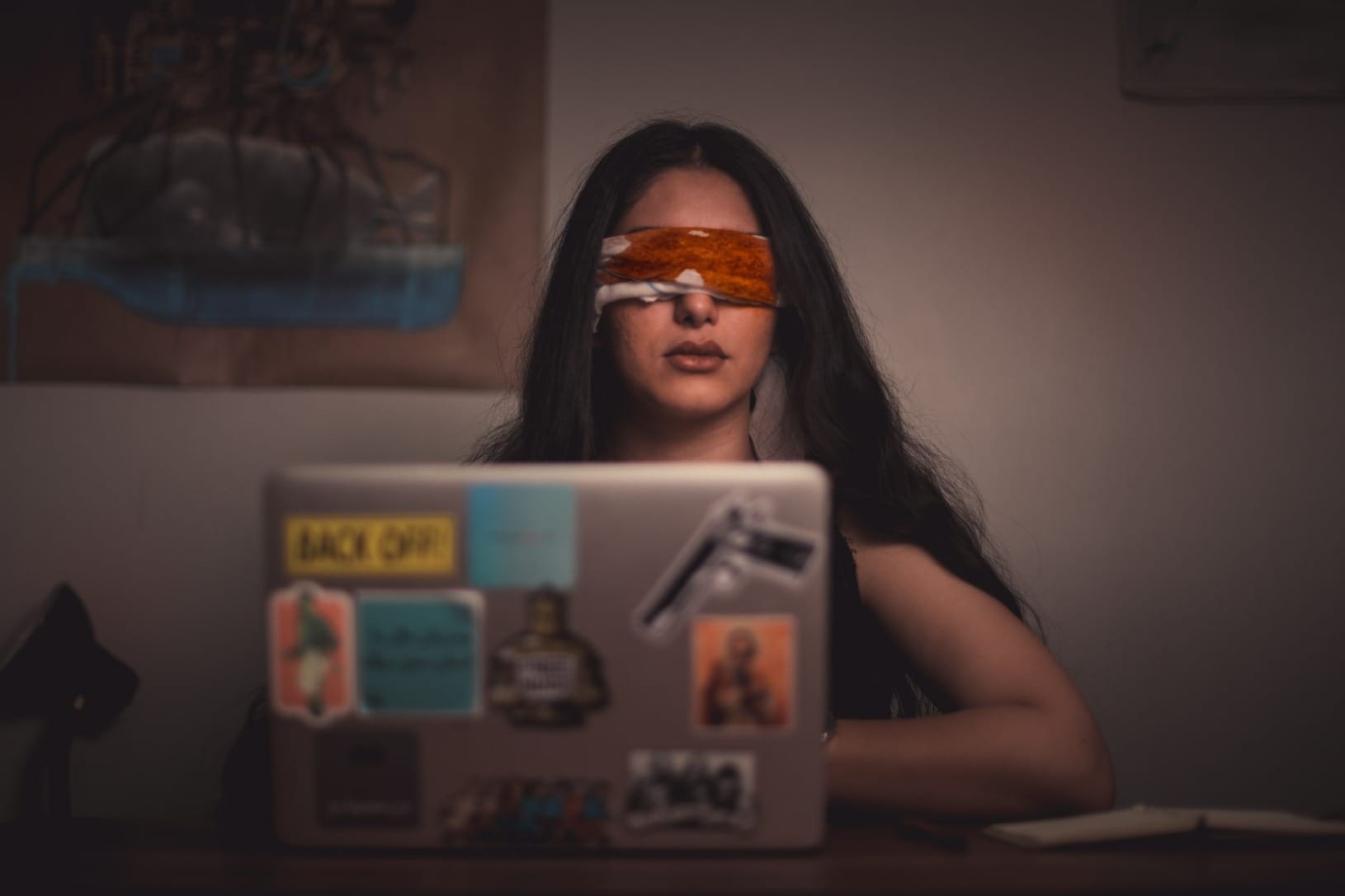 woman with blindfold sitting in front of a laptop