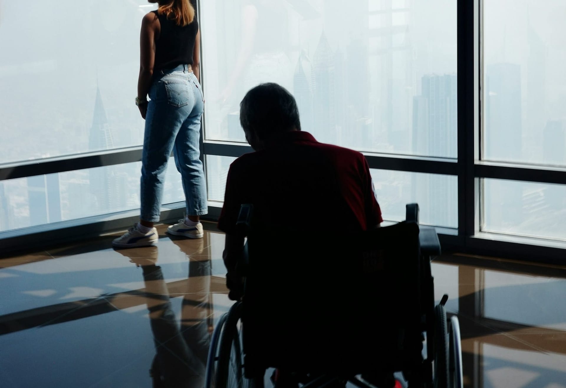 Ritratto di un uomo su sedia a rotelle con ragazza che guarda fuori dalla finestra, in un ambiente sereno e accogliente